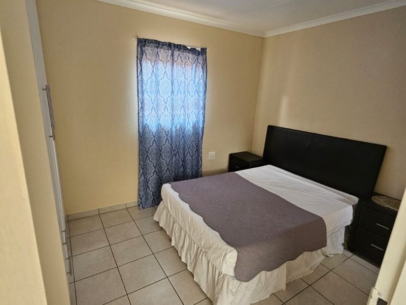A functional bedroom featuring tiled flooring, a built-in wardrobe, and neutral wall finishes, providing a clean and simple living space.