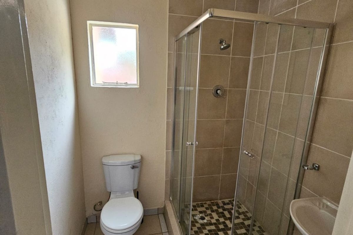 A functional bathroom featuring a glass shower enclosure, pedestal basin, and toilet with neutral floor and wall tiling.