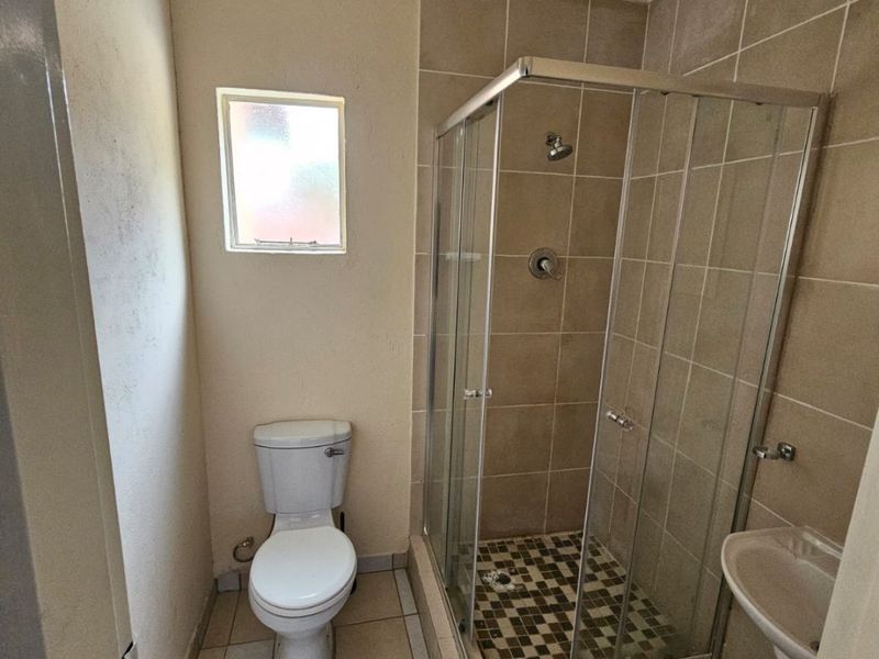 A functional bathroom featuring a glass shower enclosure, pedestal basin, and toilet with neutral floor and wall tiling.