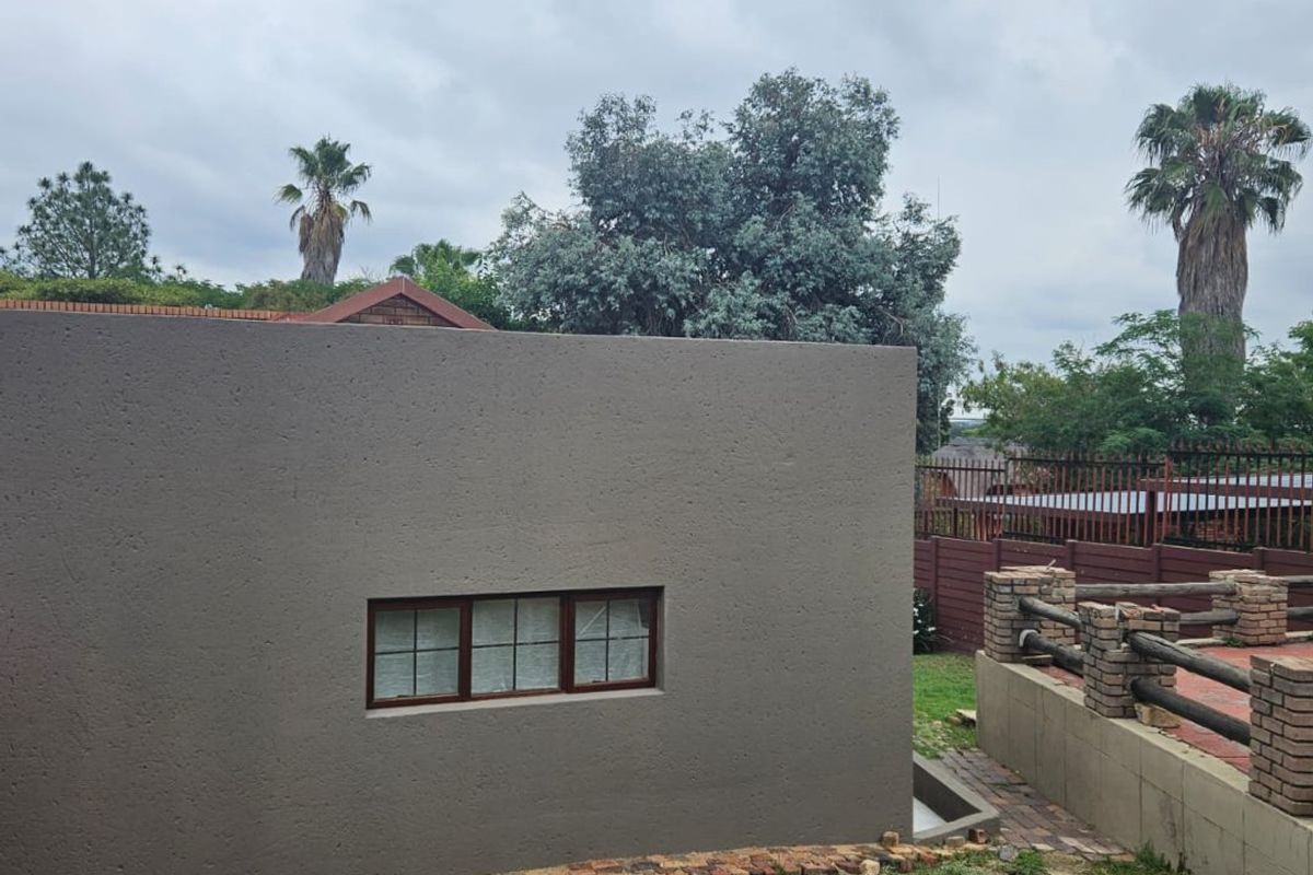 Rear exterior view of the property featuring a textured wall, multi-pane window, and a paved patio area with brick retaining walls.