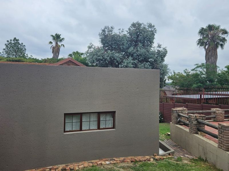 Rear exterior view of the property featuring a textured wall, multi-pane window, and a paved patio area with brick retaining walls.