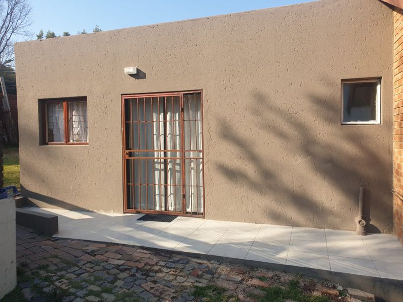 Rear exterior view of the apartment featuring a tiled patio area, security gate, and textured wall finish.