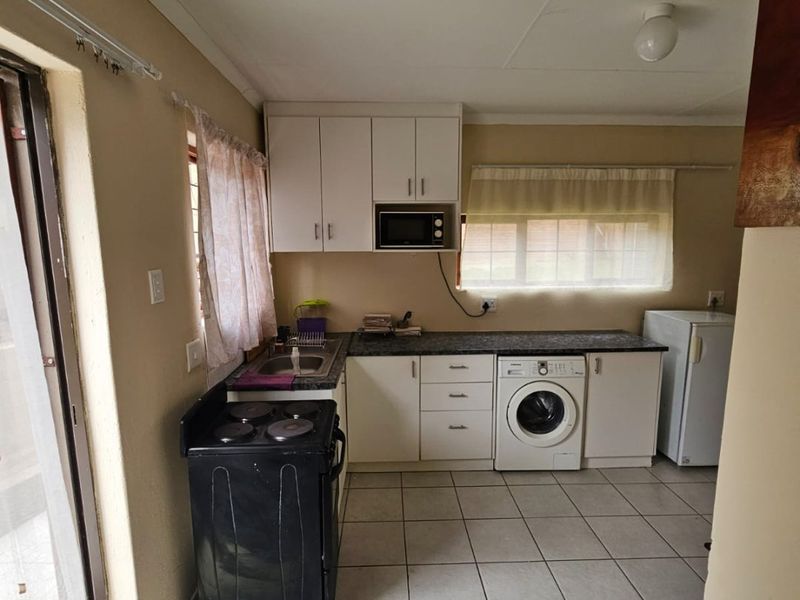 Functional kitchen featuring white cabinetry, laminate countertops, tiled flooring, and integrated laundry plumbing, offering a practical layout for daily use.