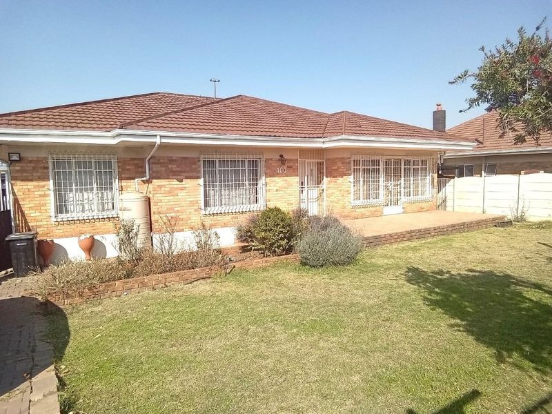 Front view of a single-story brick house featuring a tiled roof, security bars on windows, and a paved patio area overlooking the front lawn.