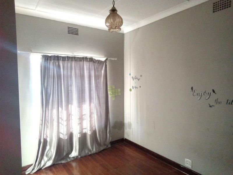 An empty bedroom featuring hardwood flooring, neutral walls with minor surface imperfections, and a classic ceiling light fixture.