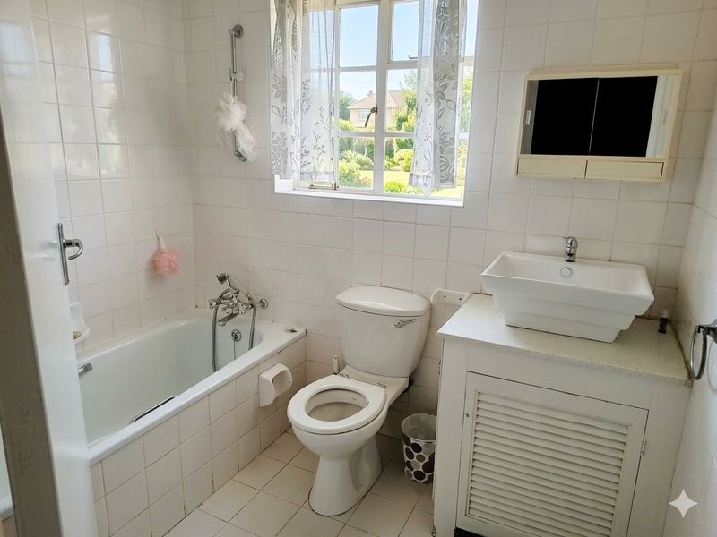 A functional bathroom featuring a built-in bathtub, toilet, and a vessel sink set on a vanity cabinet with tiled finishes throughout.