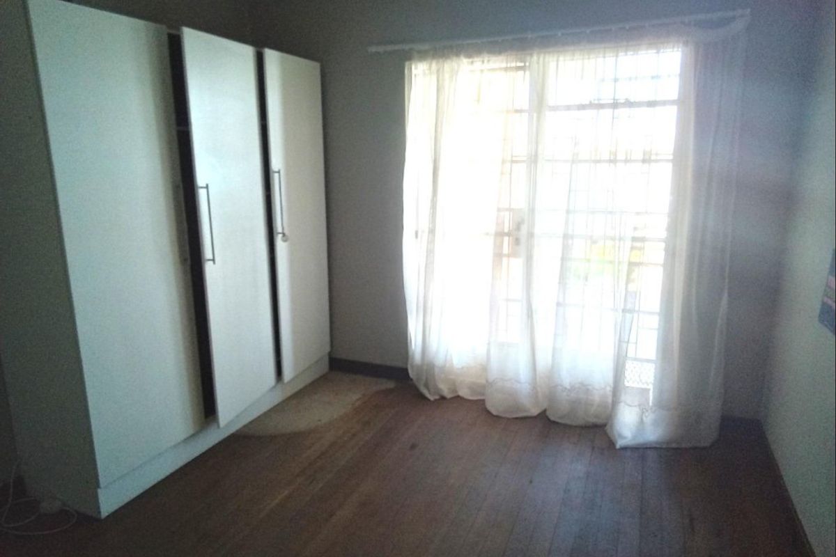 A vacant bedroom featuring timber flooring, built-in cupboards, and a sliding glass door with access to the exterior.