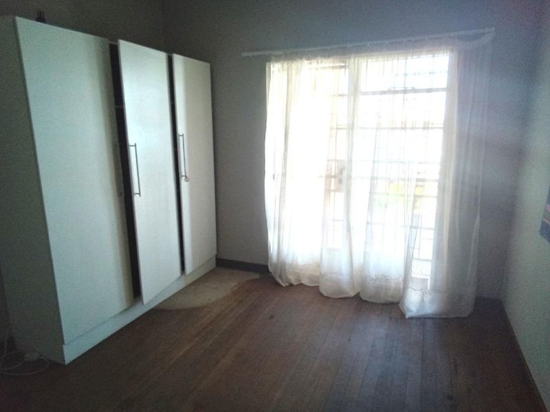 A vacant bedroom featuring timber flooring, built-in cupboards, and a sliding glass door with access to the exterior.