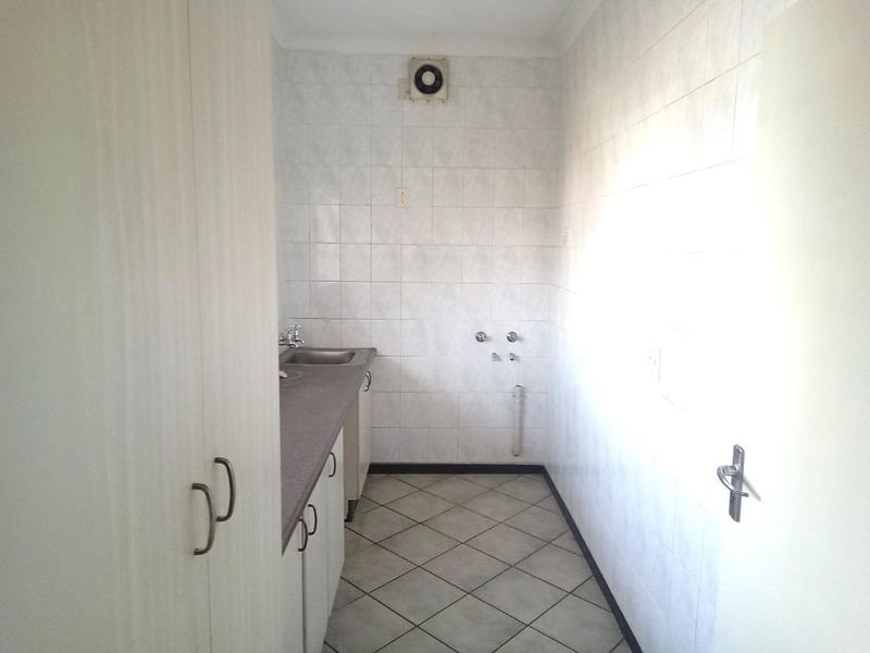 A functional laundry room featuring tiled walls and flooring, built-in cabinetry, a stainless steel sink, and dedicated plumbing connections for appliances.