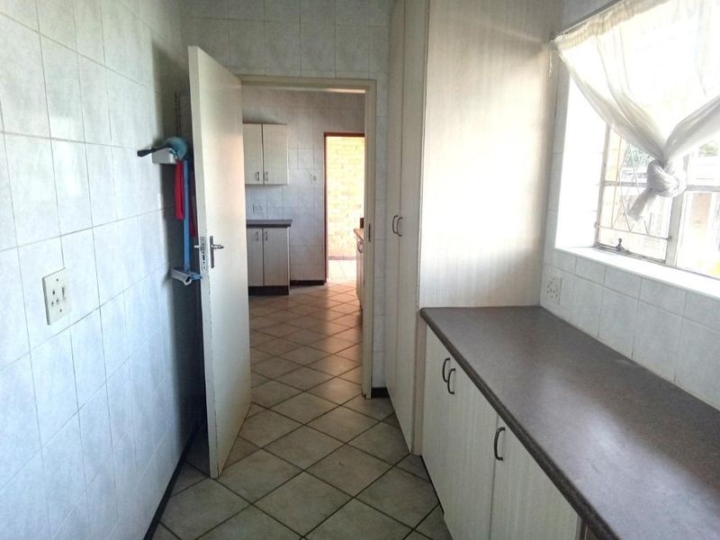 A functional scullery area featuring tiled walls, built-in cabinetry with laminate countertops, and tiled flooring, providing additional prep and storage space.