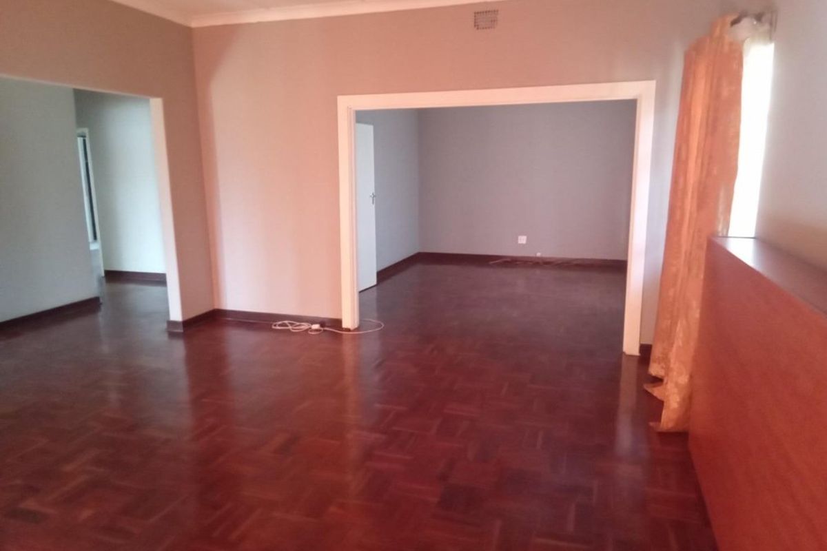 Spacious living area featuring classic parquet flooring and an open-plan layout with connecting archways, providing a versatile blank canvas for interior design.