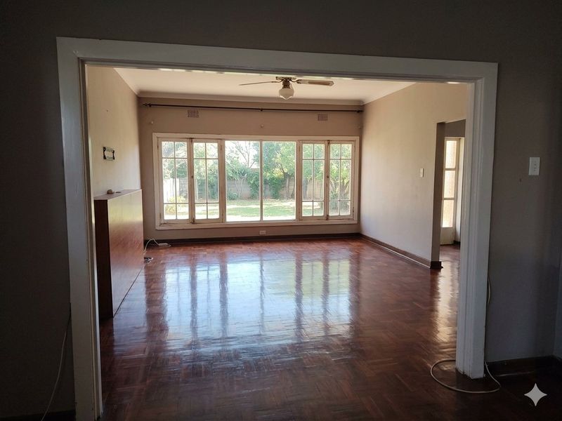 Spacious living area featuring original parquet flooring, a ceiling fan, and large windows providing natural light and garden views.