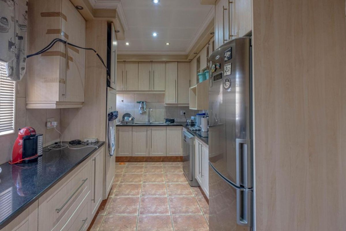 A functional galley-style kitchen featuring light wood cabinetry, dark granite countertops, tiled flooring, and recessed lighting.