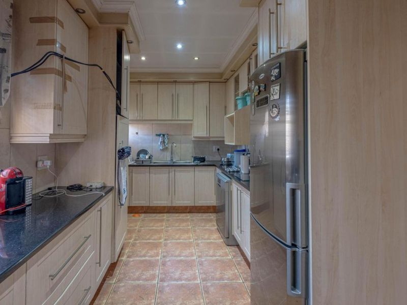 A functional galley-style kitchen featuring light wood cabinetry, dark granite countertops, tiled flooring, and recessed lighting.