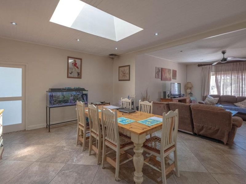 Spacious open-plan living and dining area featuring tiled flooring, a large skylight, and a ceiling fan, creating a bright and functional family space.