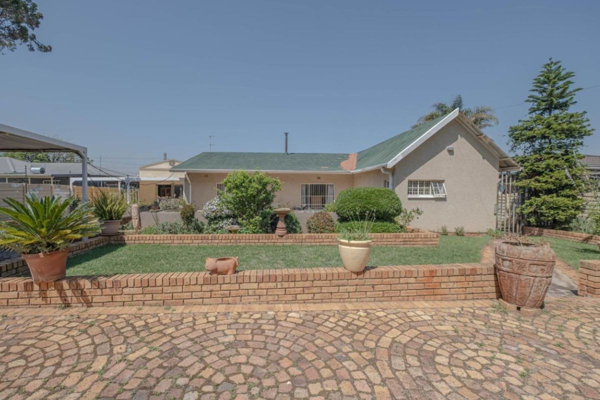 Rear view of the property featuring a brick paved driveway, tiered garden with brick retaining walls, and a corrugated metal roof.