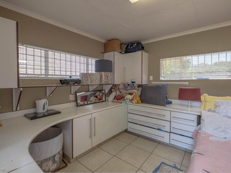 A functional scullery or utility area featuring built-in white cabinetry, laminate countertops, and tiled flooring, with security bars installed on the windows.