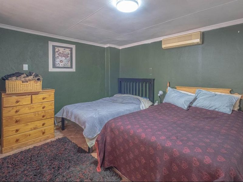 A bedroom featuring tiled flooring, a wall-mounted air conditioning unit, and built-in storage, with dark green painted walls.