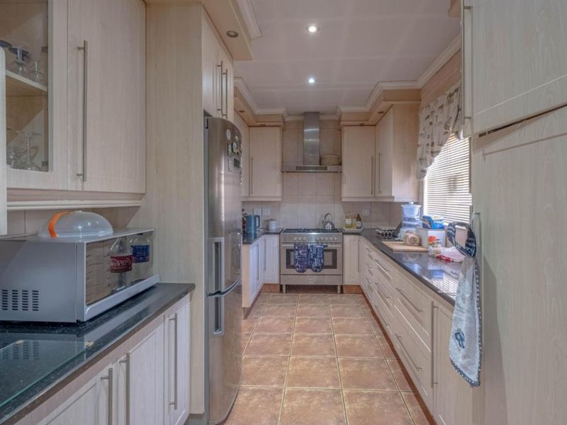 A functional galley-style kitchen featuring light wood cabinetry, granite countertops, tiled flooring, and stainless steel appliances.
