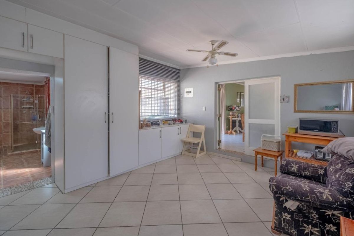 A bedroom featuring tiled flooring, built-in cupboards, a ceiling fan, and direct access to an en-suite bathroom and adjacent living area.