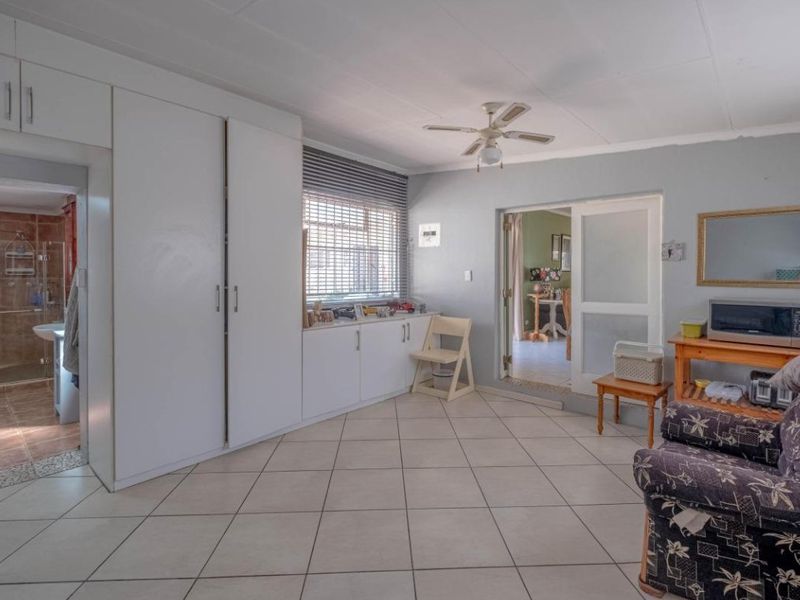 A bedroom featuring tiled flooring, built-in cupboards, a ceiling fan, and direct access to an en-suite bathroom and adjacent living area.