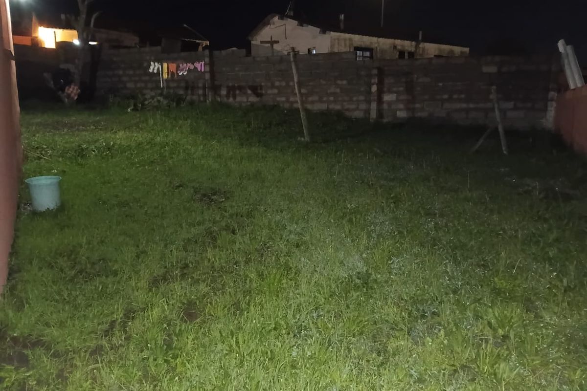 A night-time view of a rear garden area featuring a grass lawn and a brick boundary wall.
