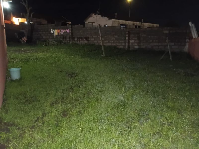 A night-time view of a rear garden area featuring a grass lawn and a brick boundary wall.