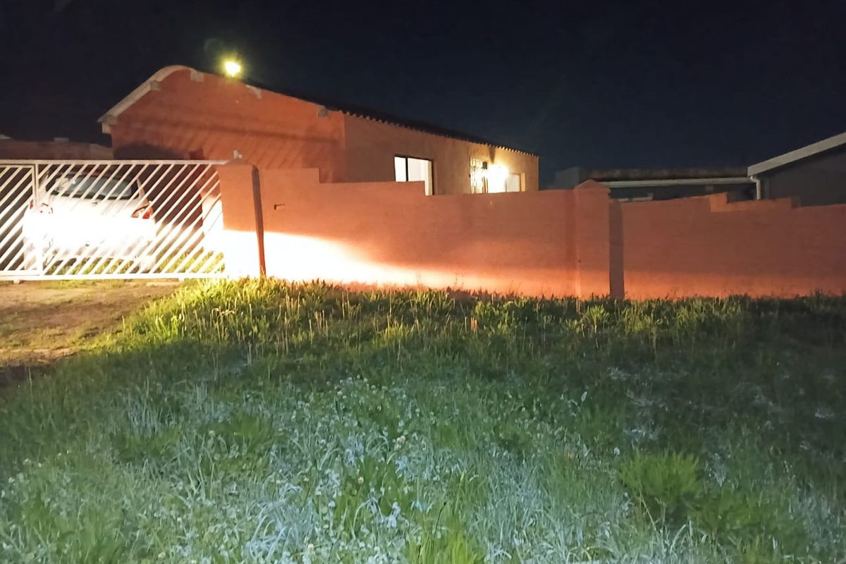 Night view of the property front elevation featuring a perimeter wall, sliding gate, and driveway access.