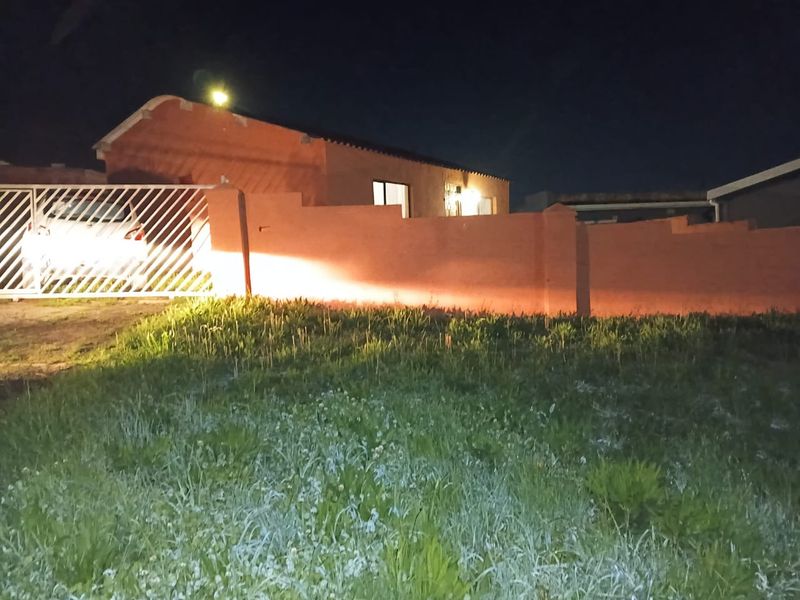 Night view of the property front elevation featuring a perimeter wall, sliding gate, and driveway access.