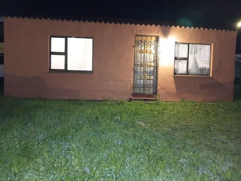 Front elevation of a single-story house at night, featuring a security gate and aluminium window frames, set against a grassed yard.