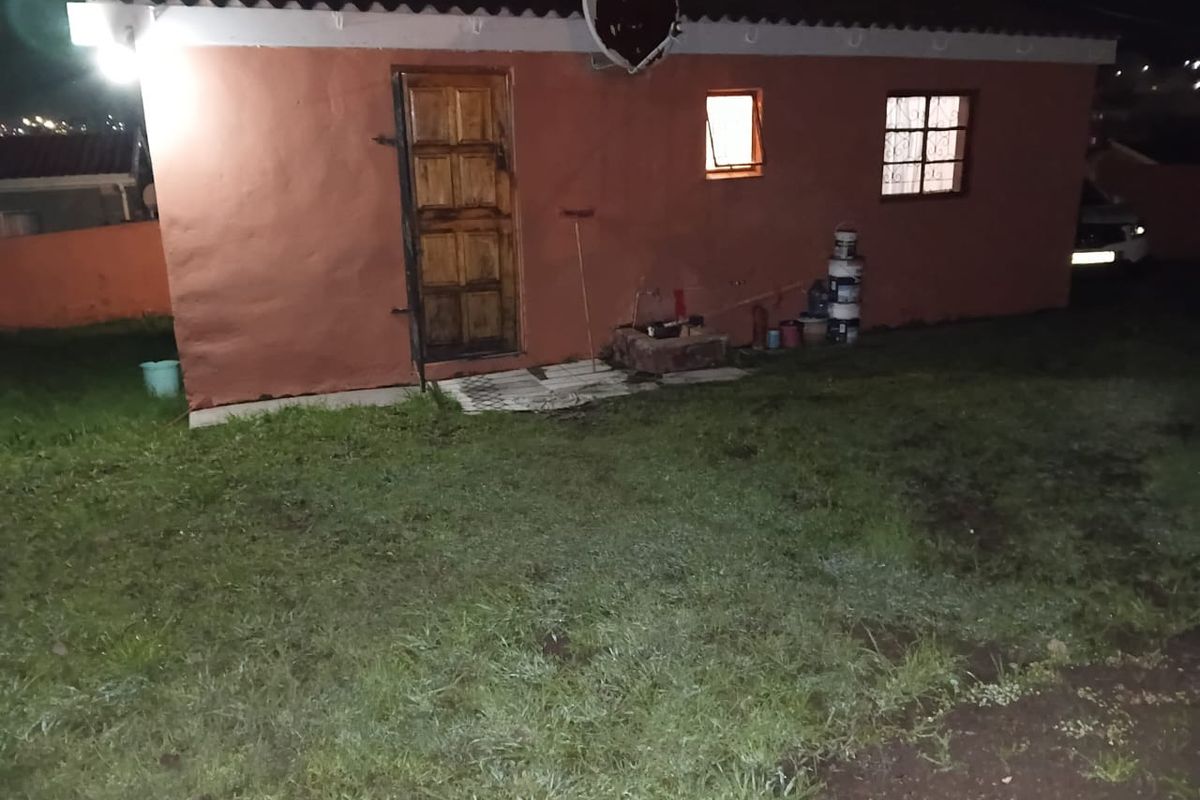A rear exterior view of a residential property featuring a timber door, security-barred windows, and a tiled roof, set against a grassed yard.