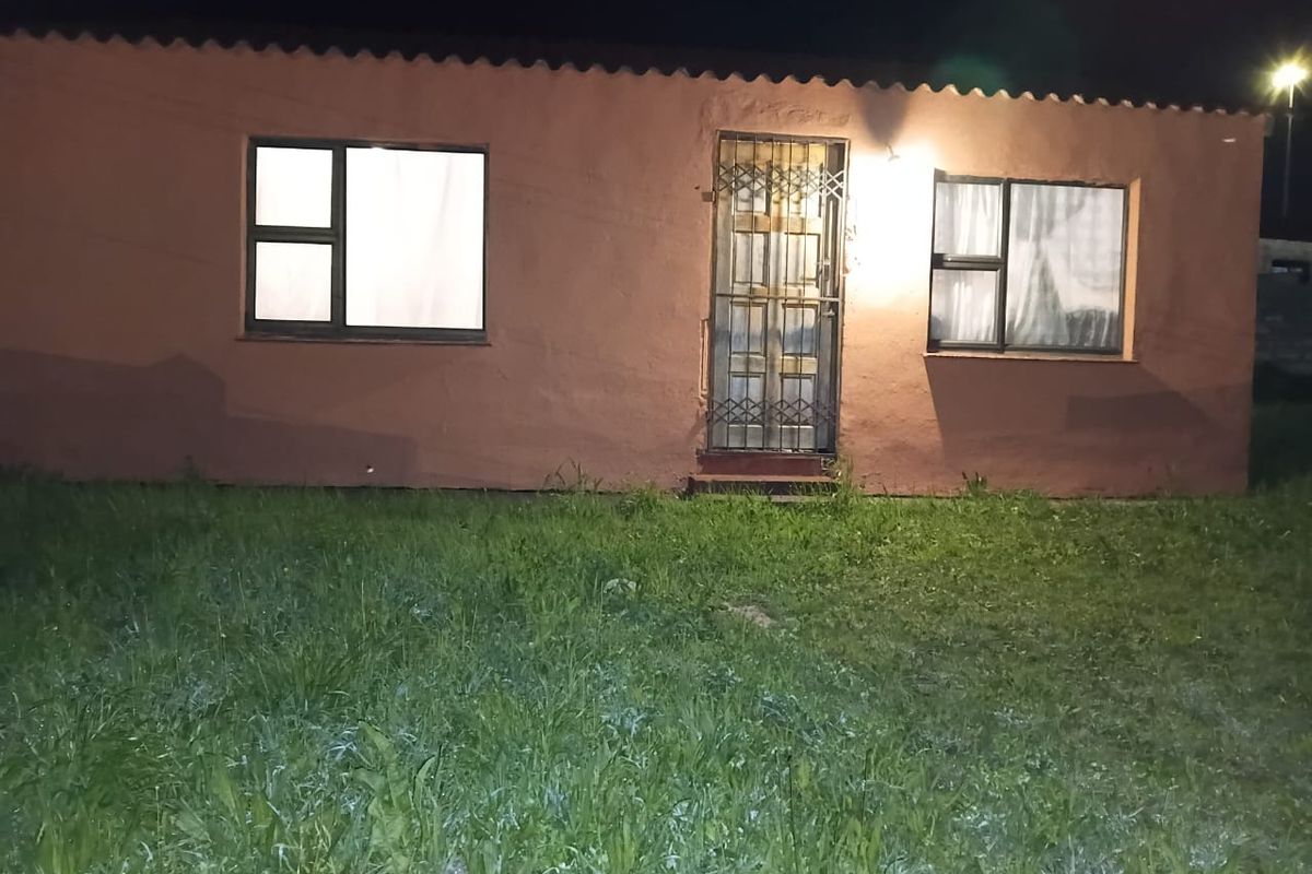Night view of the front facade featuring a security gate and aluminium window frames, set against a lawn area.
