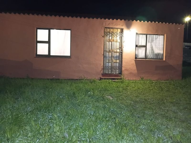 Night view of the front facade featuring a security gate and aluminium window frames, set against a lawn area.