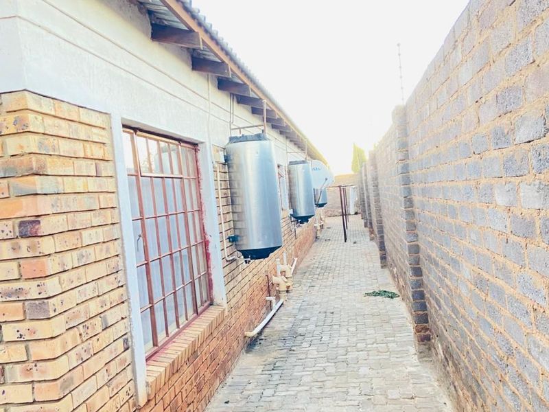 A narrow side passage featuring brick paving, perimeter walling, and multiple wall-mounted electric geysers along the building exterior.