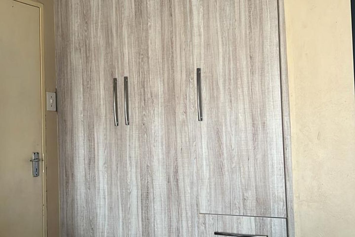 A bedroom featuring light wood-grain built-in cupboards with modern handles, recessed ceiling lighting, and decorative crown molding.