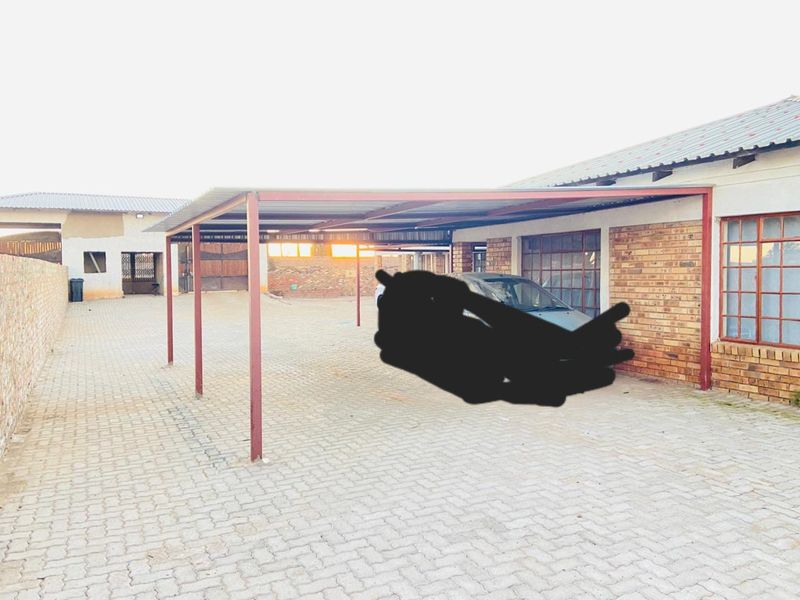 Exterior view of a commercial property featuring a large paved driveway, a covered carport structure, and facebrick exterior walls.