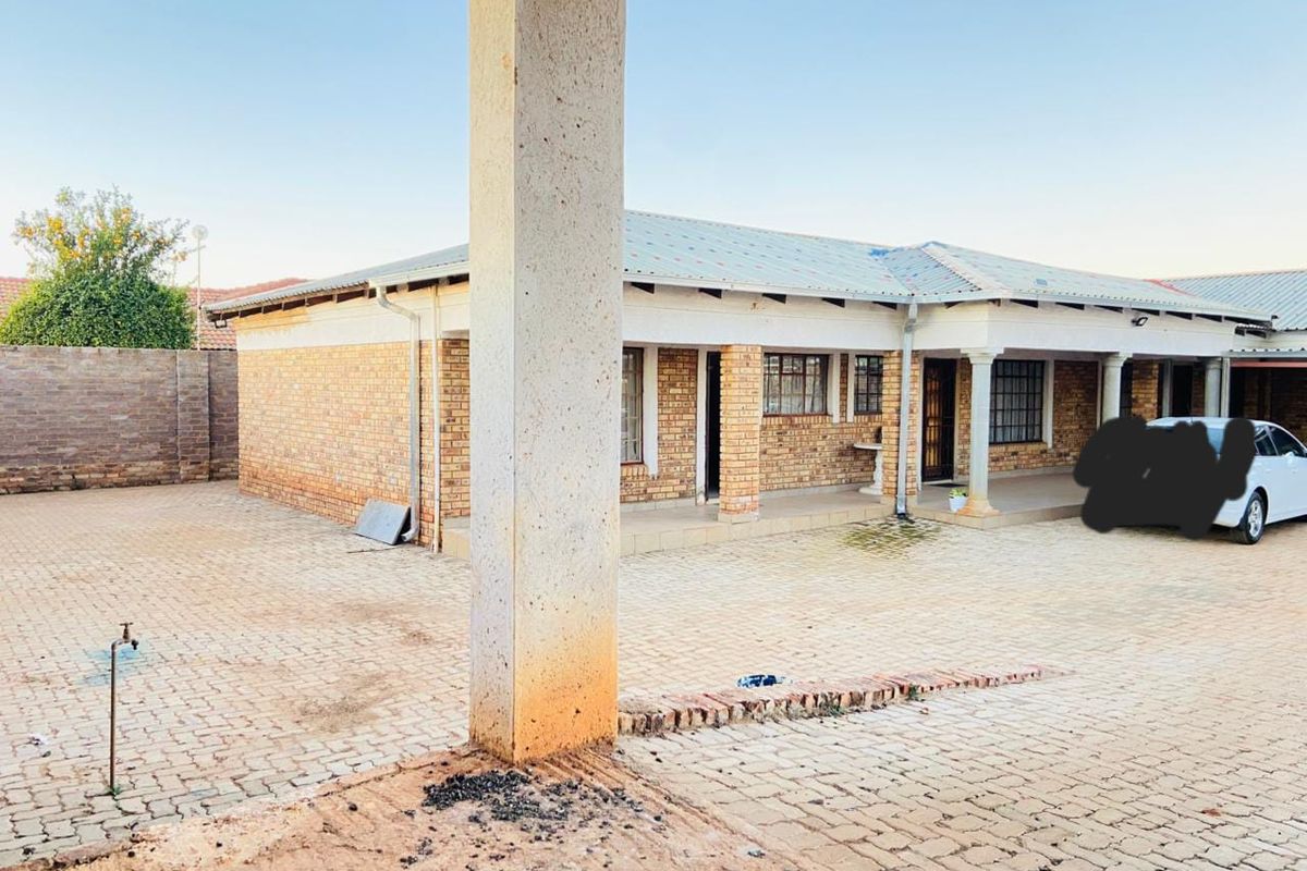 Rear exterior view of a face brick commercial property featuring a paved courtyard, covered patio area, and concrete structural columns.