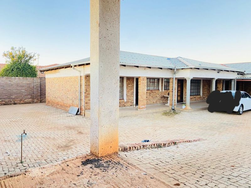 Rear exterior view of a face brick commercial property featuring a paved courtyard, covered patio area, and concrete structural columns.