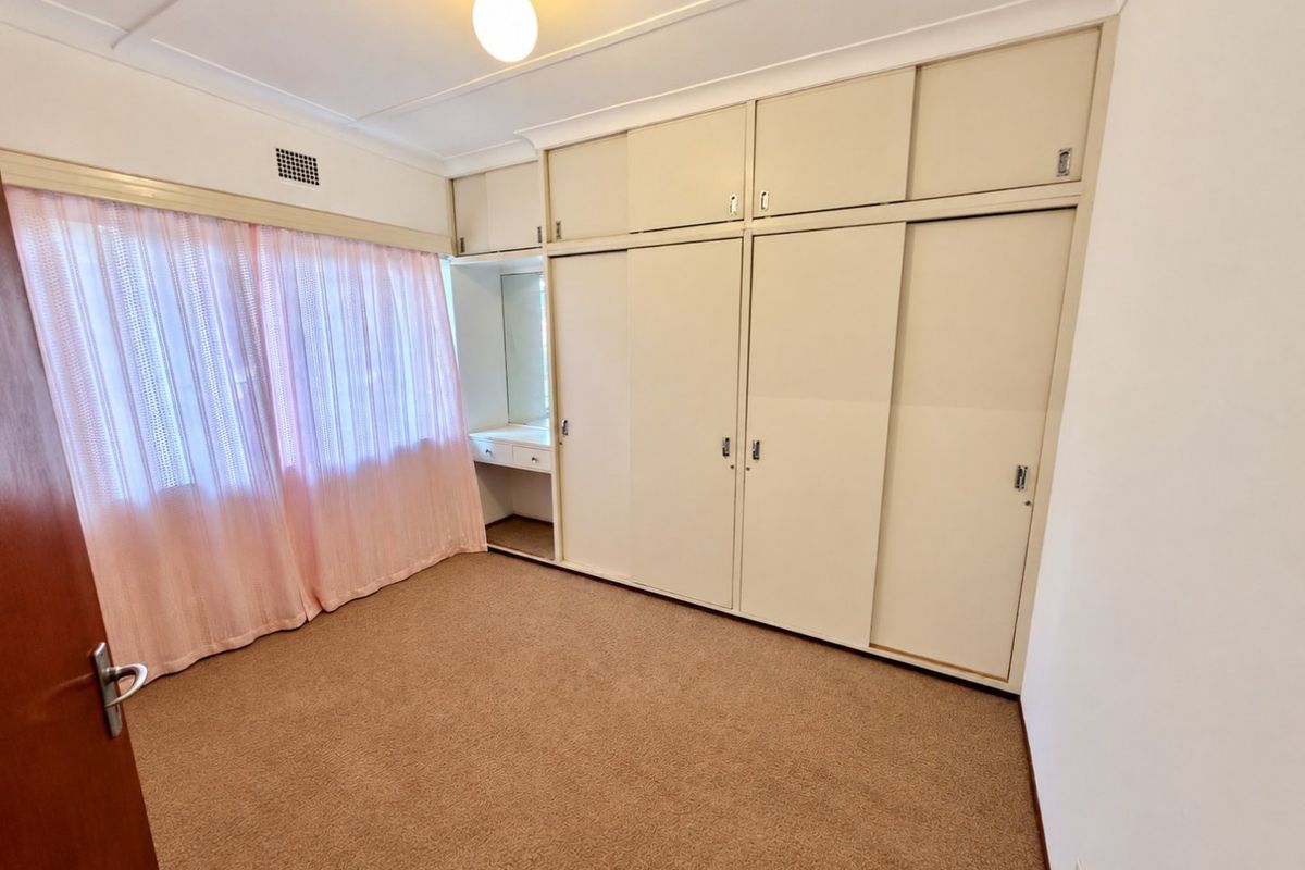 A bedroom featuring built-in wardrobes with an integrated vanity unit, carpeted flooring, and neutral wall finishes.