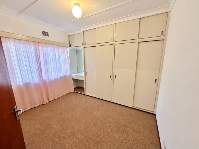 A bedroom featuring built-in wardrobes with an integrated vanity unit, carpeted flooring, and neutral wall finishes.
