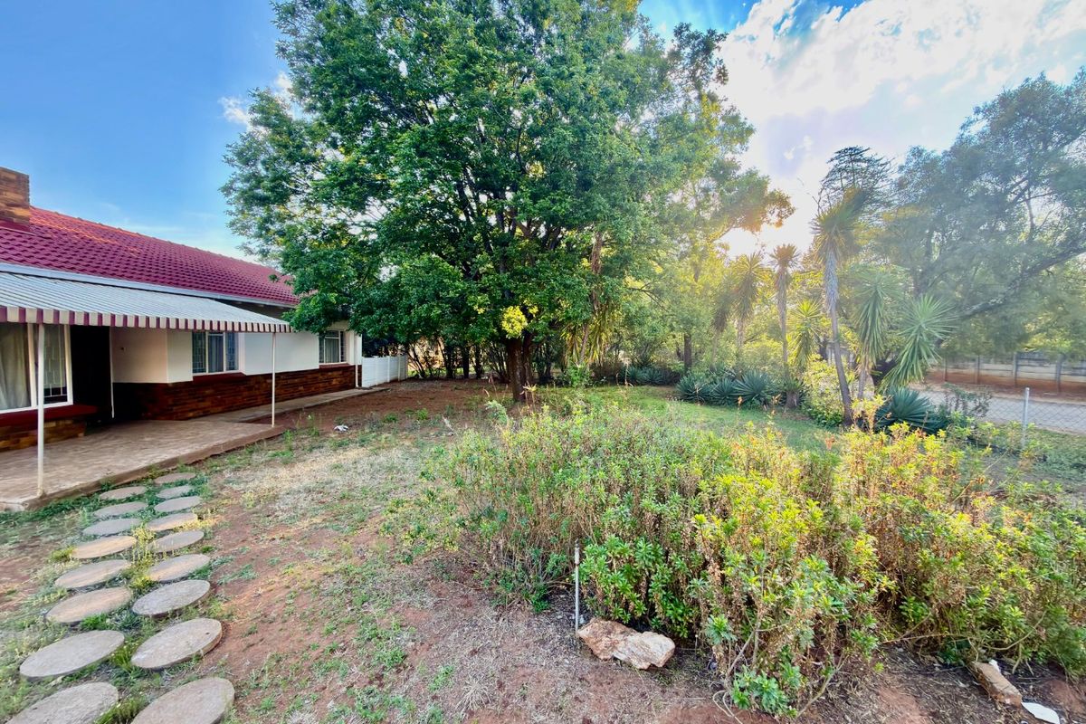 A spacious rear garden featuring a covered patio area, mature trees, and a stone pathway leading through the landscaped yard.
