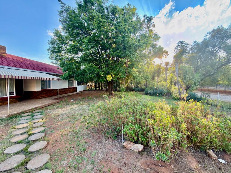 A spacious rear garden featuring a covered patio area, mature trees, and a stone pathway leading through the landscaped yard.