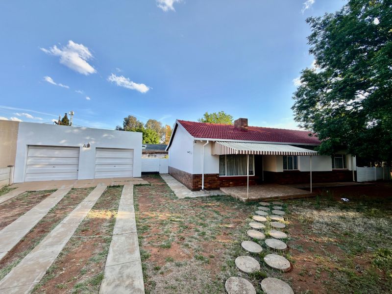 Front view of a single-story house featuring a double garage, tiled roof, and a covered patio area with a paved walkway.