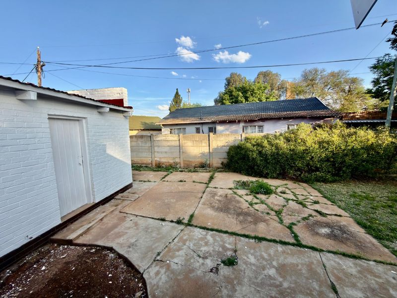 Rear exterior area featuring a concrete paved patio, precast boundary wall, and access to a painted brick outbuilding.