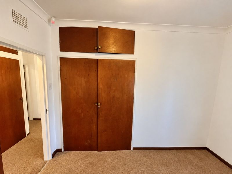 An empty bedroom featuring built-in wooden wardrobes with overhead storage, carpeted flooring, and coved ceilings.