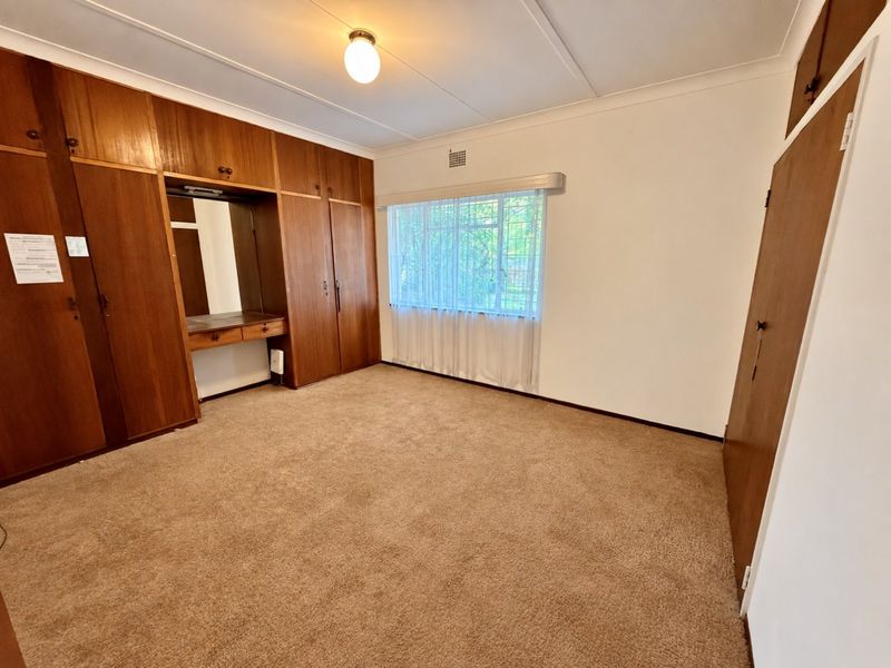 A spacious bedroom featuring extensive built-in wooden cabinetry with an integrated vanity, carpeted flooring, and a window fitted with security bars.