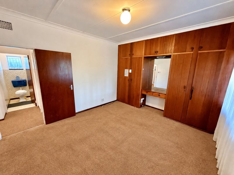 A spacious bedroom featuring extensive built-in wooden cabinetry with an integrated vanity mirror, carpeted flooring, and direct access to an en-suite bathroom.