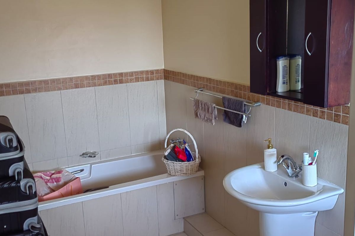 A functional bathroom featuring a bathtub, pedestal basin, and wall-mounted storage cabinet with neutral wall tiling and a decorative border.