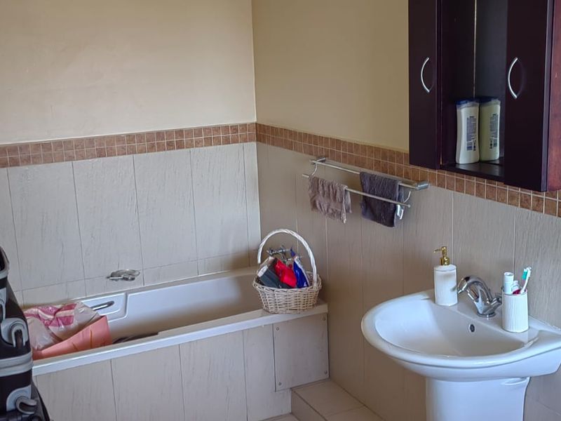 A functional bathroom featuring a bathtub, pedestal basin, and wall-mounted storage cabinet with neutral wall tiling and a decorative border.