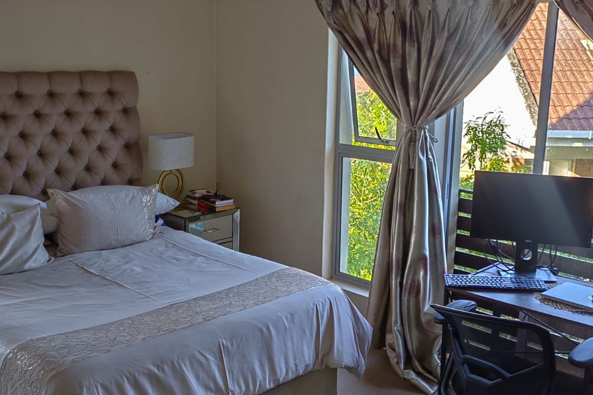 A well-lit bedroom featuring neutral walls, carpeted flooring, and large aluminium-framed windows that provide natural light and access to an outdoor balcony area.